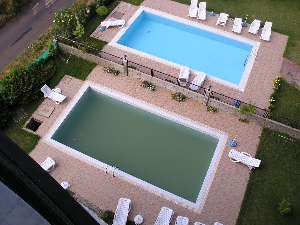 A swimming pool with blue water next to a swimming pool with green water.