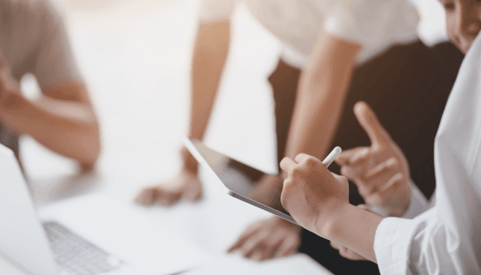 Alation Blog Image: A close-up image capturing a group meeting where an individual is using an iPad to demonstrate collaborative teamwork within a data governance team.