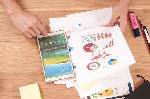 Overhead view of a person's hand holding a smartphone while reviewing data sheets and examining data quality metrics.