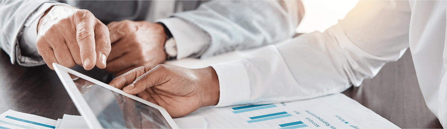 A zoomed up shot of two business people holding an Ipad while datasheets are on top of their desk