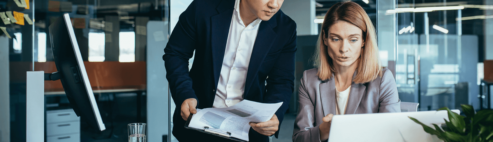 Alation Blog Image: Two business people in an office setting looking at their laptops reading about data catalog and master data management.