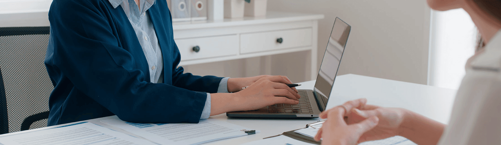 A business woman smiling as she types on her laptop while chatting with a customer