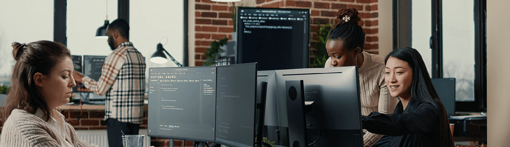 Alation Image: Two data governance colleagues in an office setting while one of them points to their desktop computer screen trying to show the other something on the screen.