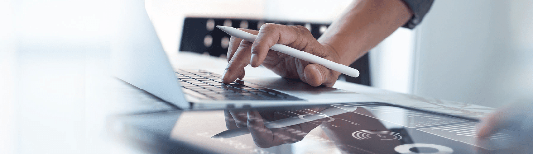 A view of a hand holding an ipad pencil while typing on their laptop computer