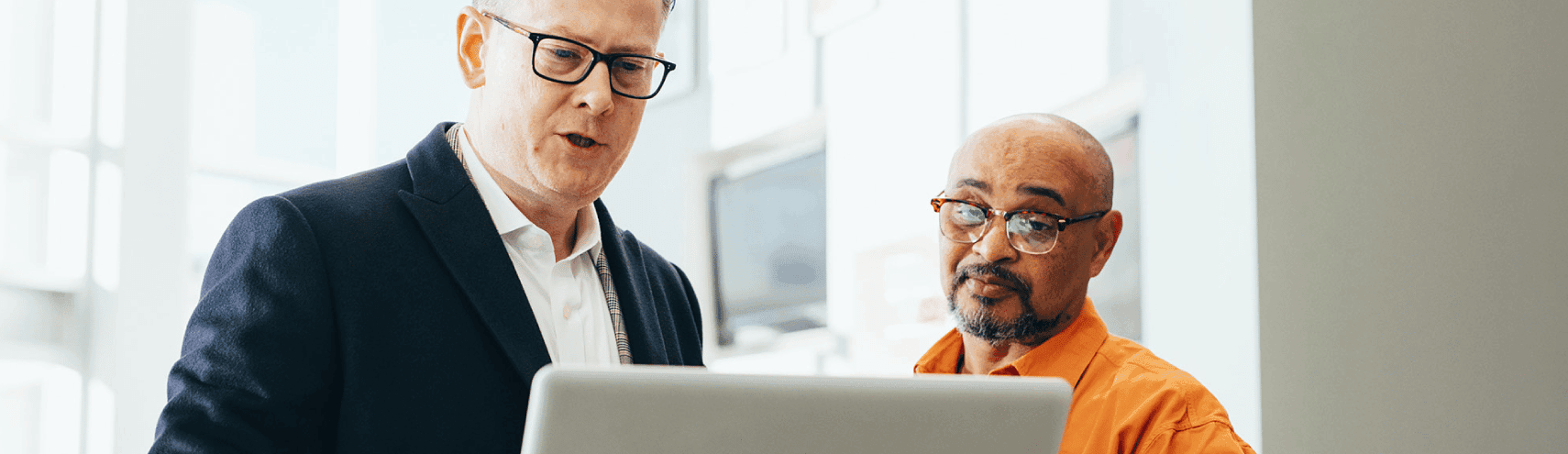 Two business colleagues discussing how to implement Alation's Data Catalog within their organization while they look into their laptops