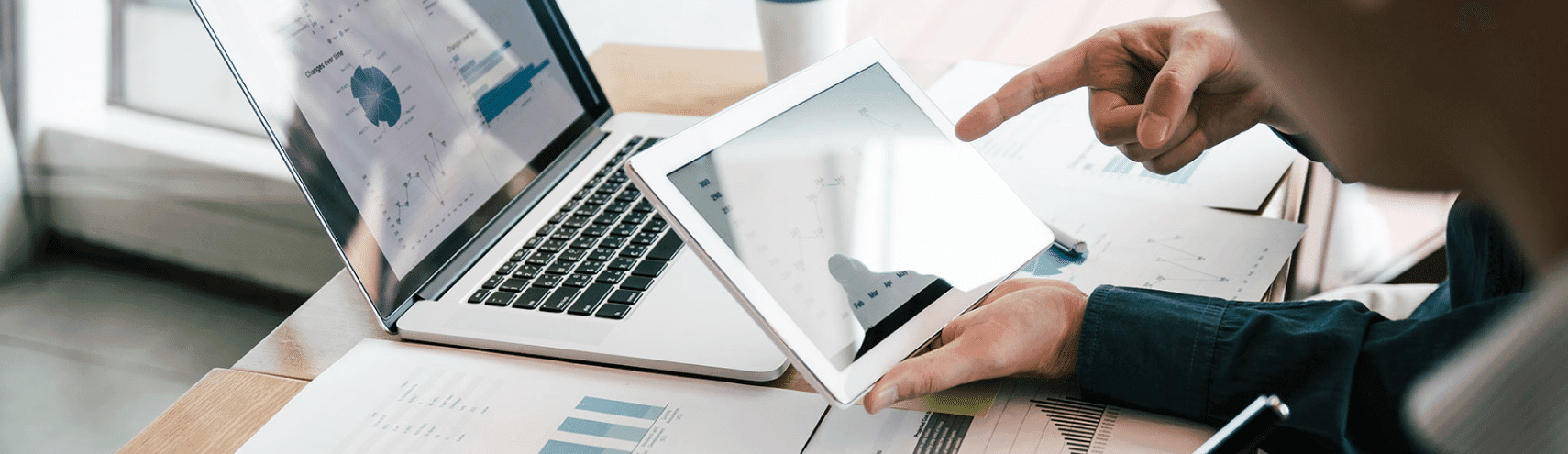 Birds-eye-view of a work desk with graphs, opened laptop, and a tablet