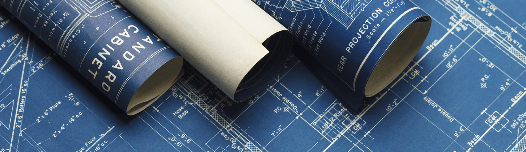 Four rolled up blueprints on top of an opened blue blueprint